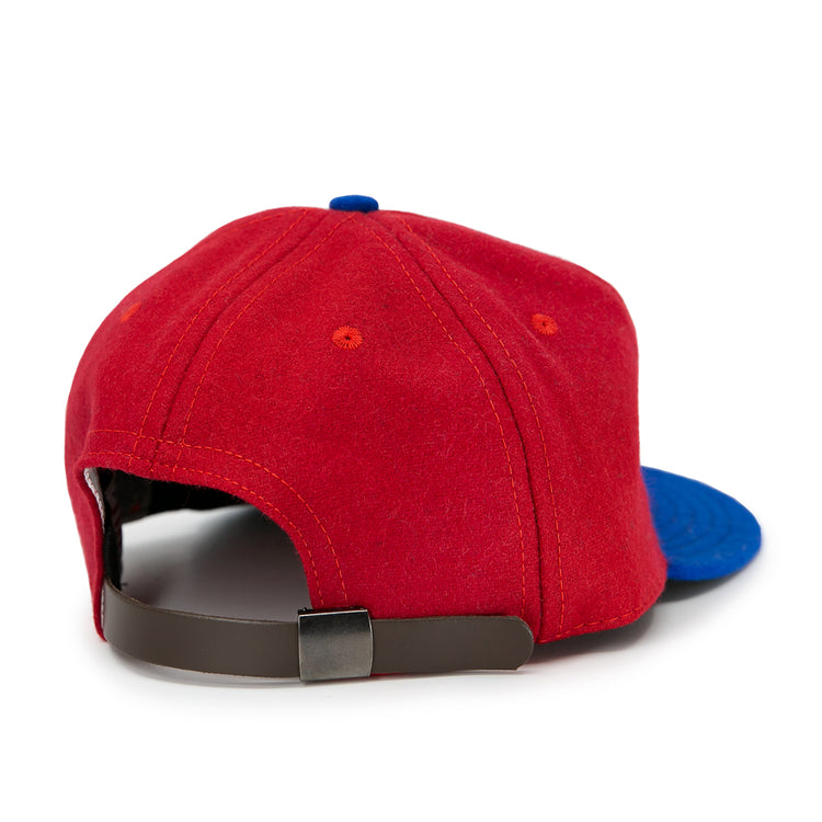The EFF Alaska Goldpanners 1964 Vintage Ballcap is red with a blue brim, shown from the back. It features an adjustable brown strap with metal clasp—an authentic reproduction of the original team cap.