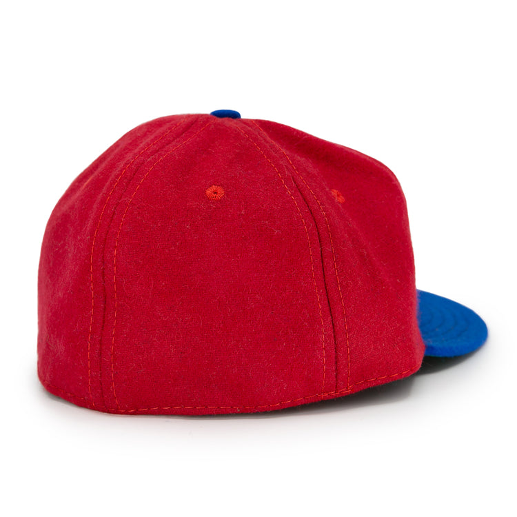 The EFF Alaska Goldpanners 1964 Vintage Ballcap is shown from the back at an angle, displaying red fabric with orange stitching and a blue brim on the right side. Authentic reproduction details are highlighted by a white background.