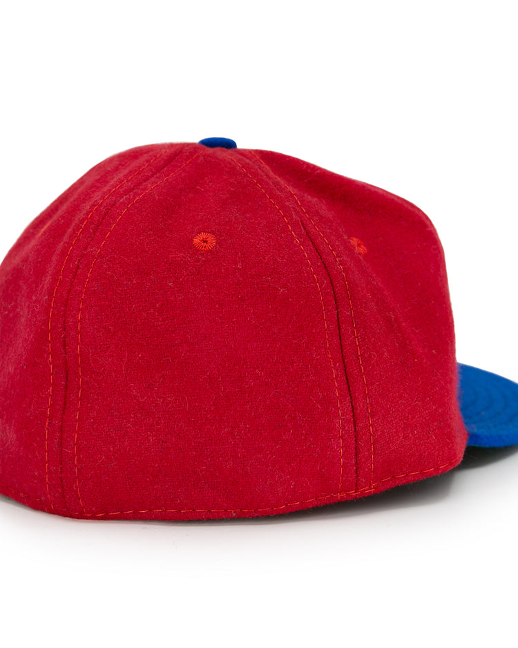 The EFF Alaska Goldpanners 1964 Vintage Ballcap is shown from the back at an angle, displaying red fabric with orange stitching and a blue brim on the right side. Authentic reproduction details are highlighted by a white background.