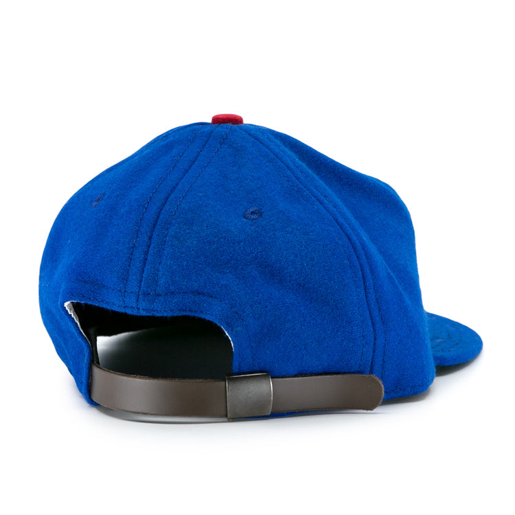 The Los Barbudos 1959 Vintage Ballcap by EFF is a blue wool cap with visible stitching, a red top button, and a brown adjustable strap with metallic clasp. The hat is shown from the back, highlighting its classic vintage details.