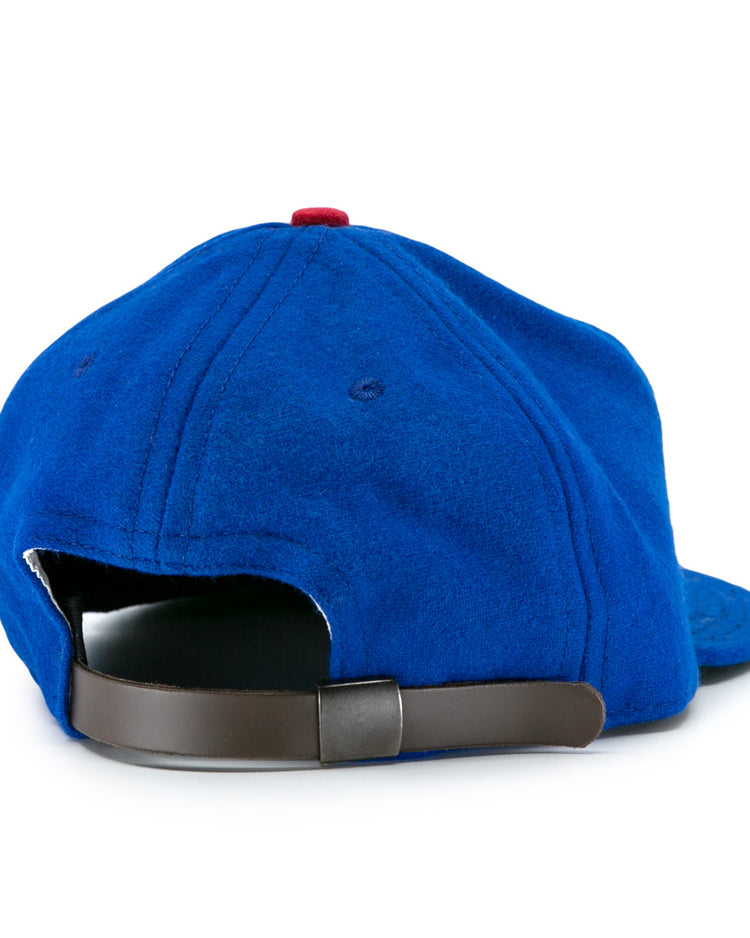 The Los Barbudos 1959 Vintage Ballcap by EFF is a blue wool cap with visible stitching, a red top button, and a brown adjustable strap with metallic clasp. The hat is shown from the back, highlighting its classic vintage details.