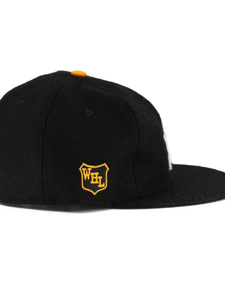 The EFF Brandon Wheat Kings 1955 Vintage Ballcap is a black wool flat-brim hat with a yellow top button and a side patch featuring a yellow and white shield with WFL, inspired by classic hockey styles.