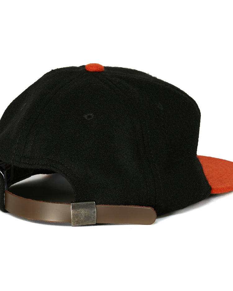 The EFF Richmond Virginians 1955 Vintage Ballcap is a black wool cap with an orange button and brim, shown from the back. It features an adjustable brown leather strap with a metal buckle, inspired by the original 1955 design.