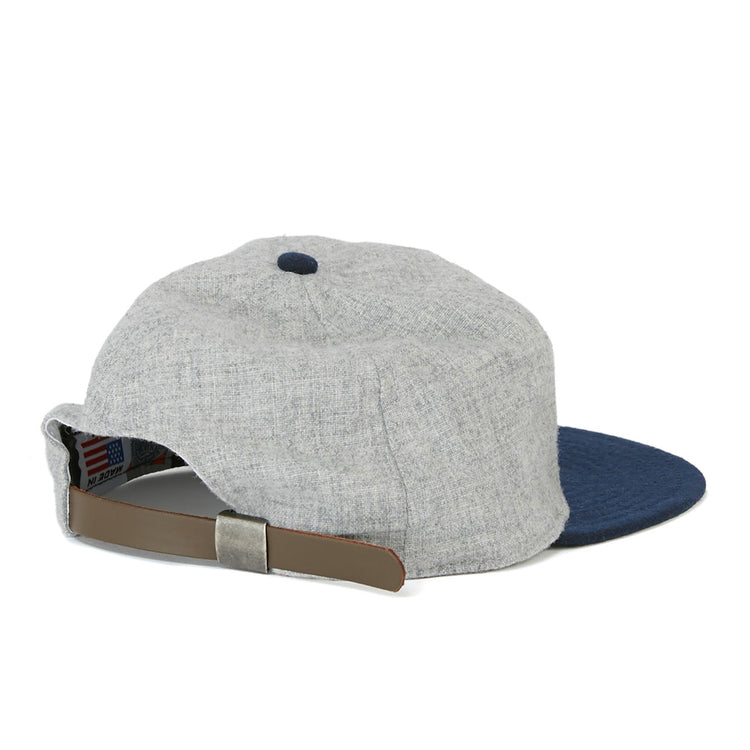 The EFF Cerveceria Caracas 1942 Vintage Ballcap is grey with a blue brim, shown from the back, and features an adjustable tan leather strap with a metal clasp, echoing classic Venezuelan League styles.
