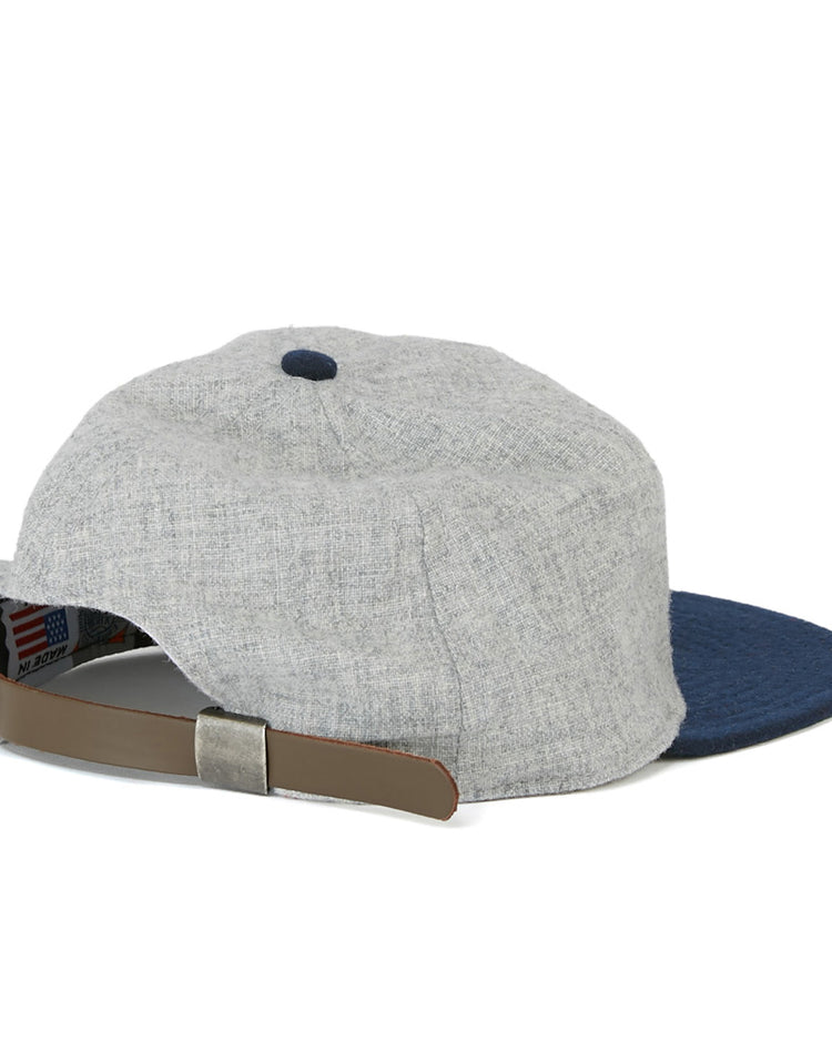 The EFF Cerveceria Caracas 1942 Vintage Ballcap is grey with a blue brim, shown from the back, and features an adjustable tan leather strap with a metal clasp, echoing classic Venezuelan League styles.