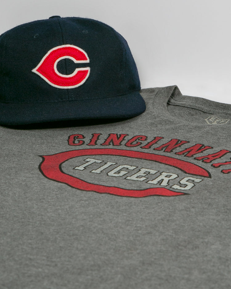 The EFF Cincinnati Tigers 1934 T-Shirt and a navy blue cap with a red and white C are displayed on a white surface, both inspired by the Negro American League.