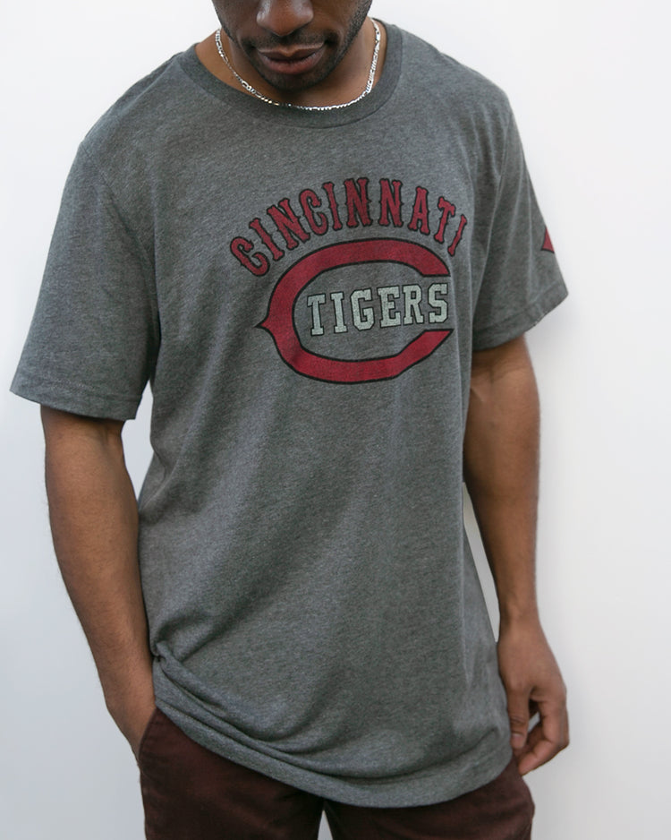 A person in an EFF Cincinnati Tigers 1934 T-Shirt, featuring red and white text on gray and a relaxed fit, stands against a white background. The historic team was once led by DeHart Hubbard; the face is partially out of frame.