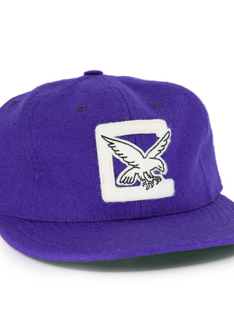 The EFF Cleveland Falcons 1936 Vintage Ballcap is a purple wool cap with a white patch and embroidered flying eagle on the front, a circular black and white logo on the side, and an adjustable leather strap for a custom fit.