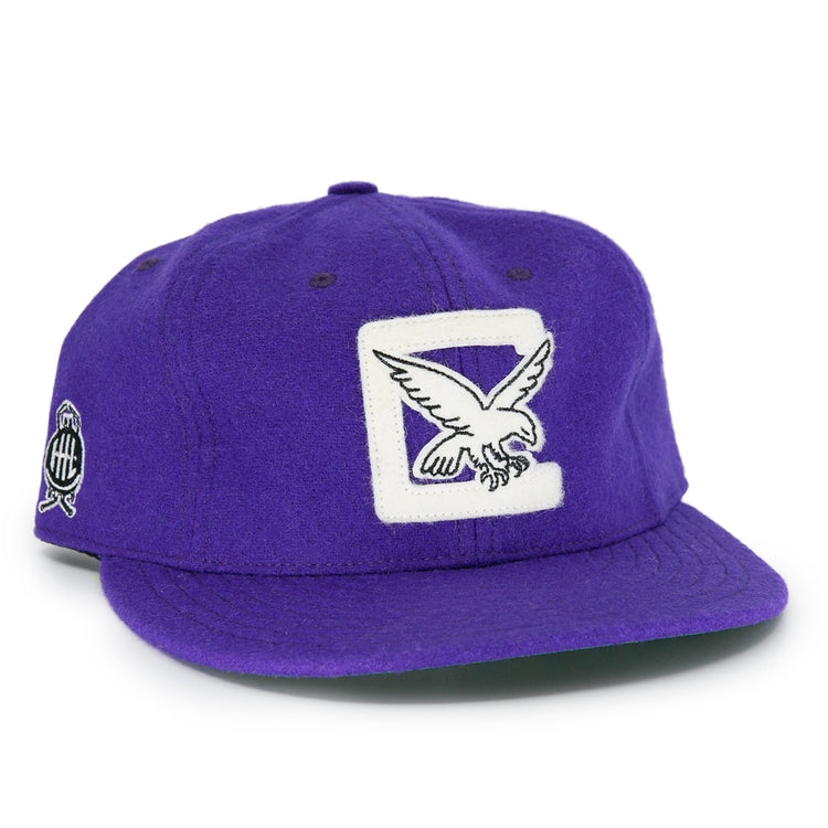 The EFF Cleveland Falcons 1936 Vintage Ballcap is a purple wool cap with a white patch and embroidered flying eagle on the front, a circular black and white logo on the side, and an adjustable leather strap for a custom fit.