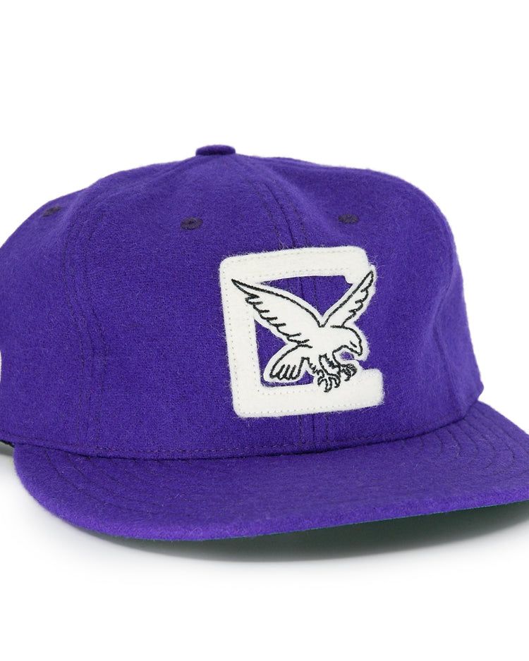 The EFF Cleveland Falcons 1936 Vintage Ballcap is a purple wool cap with a white patch and embroidered flying eagle on the front, a circular black and white logo on the side, and an adjustable leather strap for a custom fit.