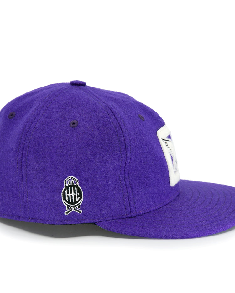 The EFF Cleveland Falcons 1936 Vintage Ballcap is a purple wool cap with a white rectangular front patch, a black and white circular side logo featuring crossed bats, and an adjustable leather strap for the perfect fit.