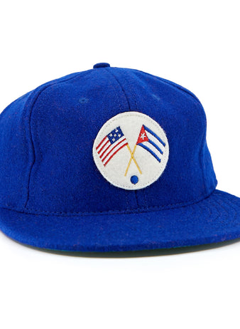 The EFF Cuban Stars 1932 Vintage Ballcap is a royal blue cap with a round white front patch featuring crossed American and Cuban flags, inspired by the East-West League’s classic design.