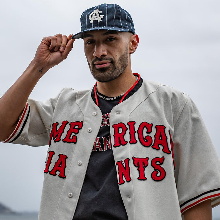 A man wearing an EFF Chicago American Giants T-Shirt with “AMERICAN GIANTS” in red lettering and a navy cap stands outdoors, honoring Negro League Black baseball history.