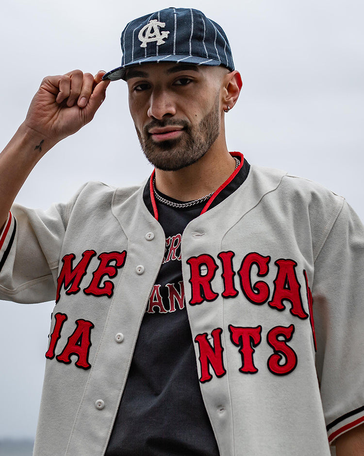 A man wearing an EFF Chicago American Giants T-Shirt with “AMERICAN GIANTS” in red lettering and a navy cap stands outdoors, honoring Negro League Black baseball history.