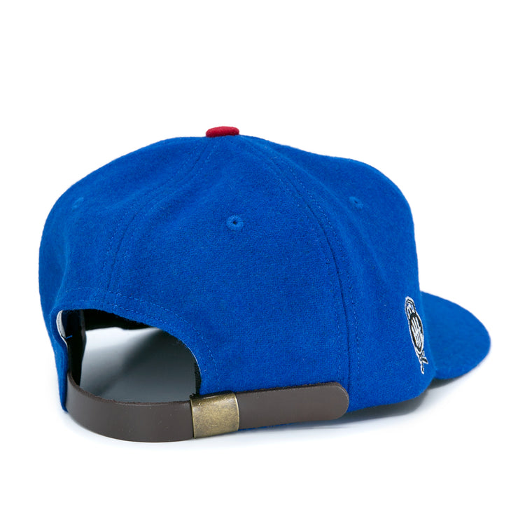 The EFF Detroit Olympics Vintage Ballcap is blue wool, shown from the back with a brown leather strap, brass clasp, a side embroidered logo, and a red top button inspired by classic International Hockey League style.