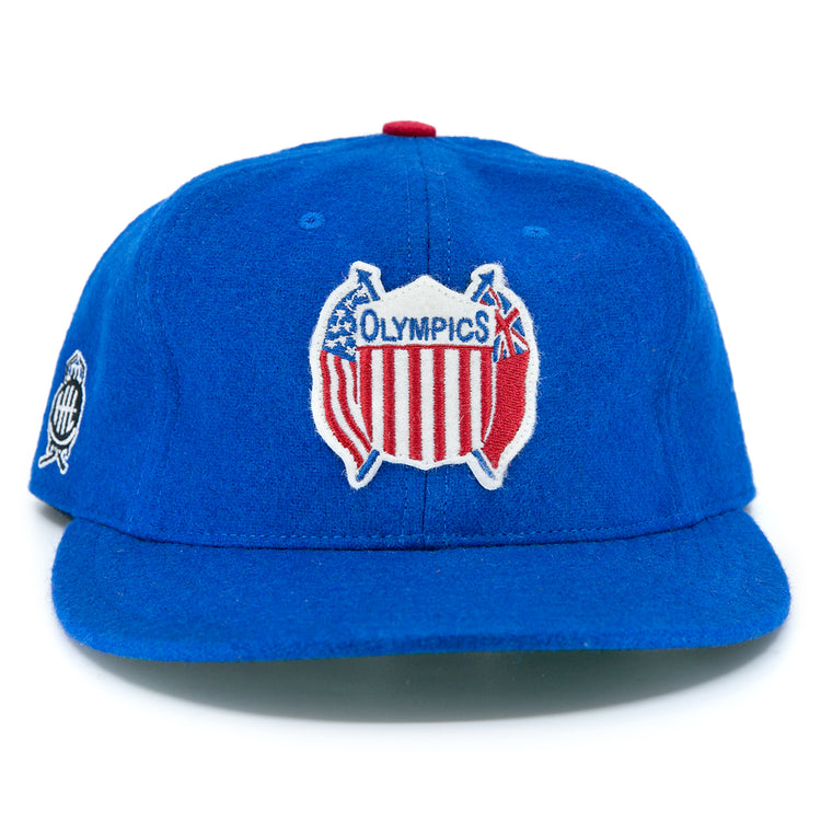 The EFF Detroit Olympics Vintage Ballcap is a royal blue wool cap with a classic Olympics logo—crossed bats and a red, white, and blue shield—plus an adjustable leather strap and an embroidered side patch.