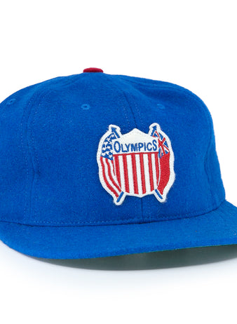 The EFF Detroit Olympics Vintage Ballcap is a blue wool cap with a red, white, and blue USA-shaped Olympic patch, a smaller white and black side patch, and an adjustable leather strap for a great fit.