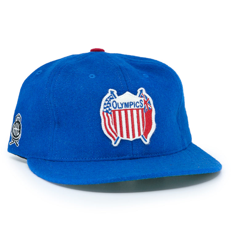 The EFF Detroit Olympics Vintage Ballcap is a blue wool cap with a red, white, and blue USA-shaped Olympic patch, a smaller white and black side patch, and an adjustable leather strap for a great fit.