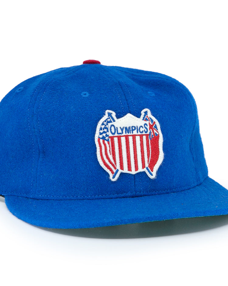 The EFF Detroit Olympics Vintage Ballcap is a blue wool cap with a red, white, and blue USA-shaped Olympic patch, a smaller white and black side patch, and an adjustable leather strap for a great fit.