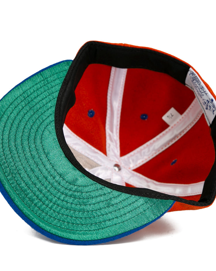 A close-up of the Ebbets Field Flannels University of Cincinnati 1960 Vintage Ballcap, featuring a green undervisor, red crown, blue accents, white seams, and sizing tag—an authentic reproduction of the classic ballcap.