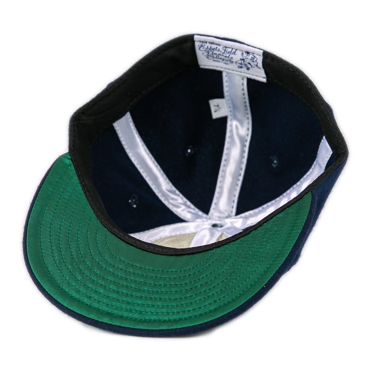 An overhead view of the Fresno State University 1958 Vintage Ballcap by Ebbets Field Flannels, featuring a green underbrim, navy blue interior, white seams, and a white label with blue text stitched into the wool headband.