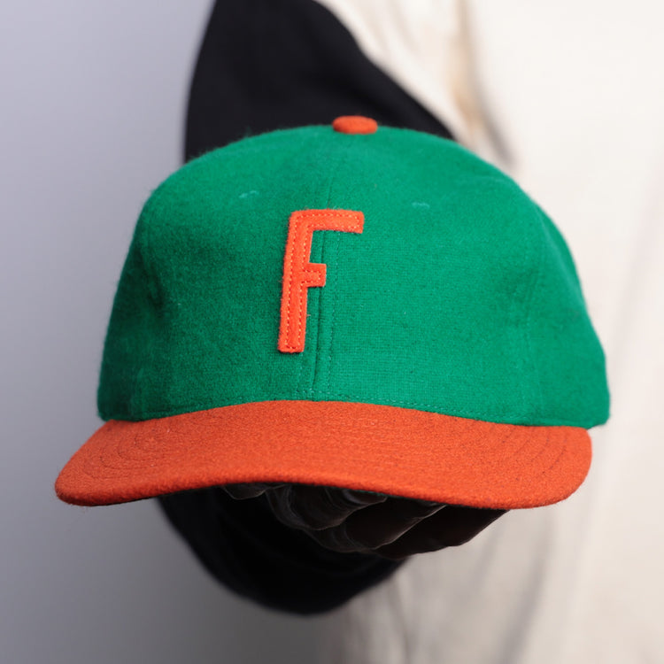 A person holds an EFF Florida A&M University 1969 Vintage Ballcap—a green cap with orange brim and “F”—against a plain background, with part of their shirt sleeve visible.
