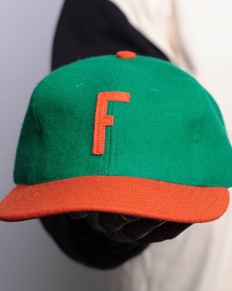 A person holds an EFF Florida A&M University 1969 Vintage Ballcap—a green cap with orange brim and “F”—against a plain background, with part of their shirt sleeve visible.