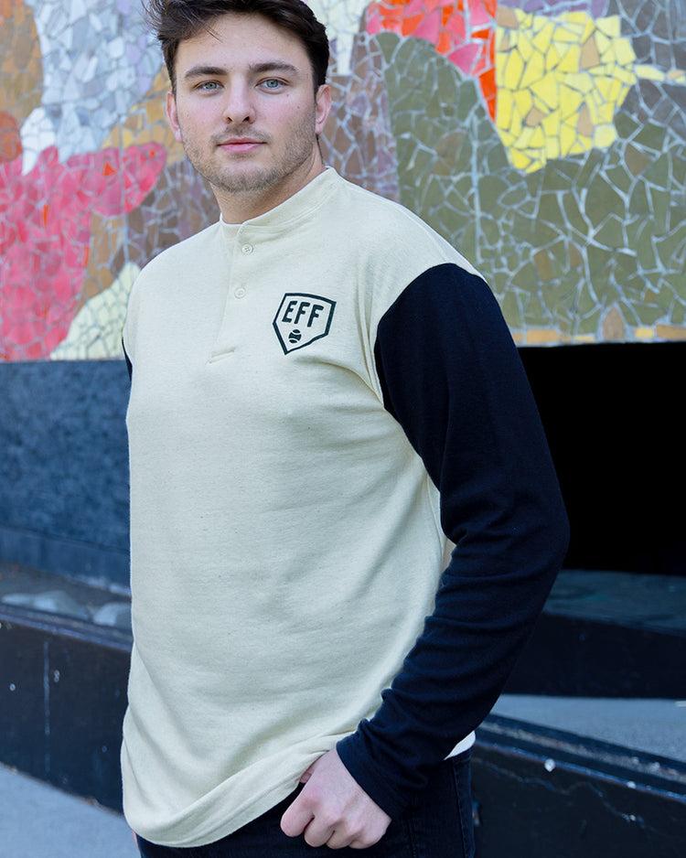 A man with short brown hair stands outdoors by a colorful mosaic wall, wearing the EFF Fungo Shirt with black sleeves and logo.