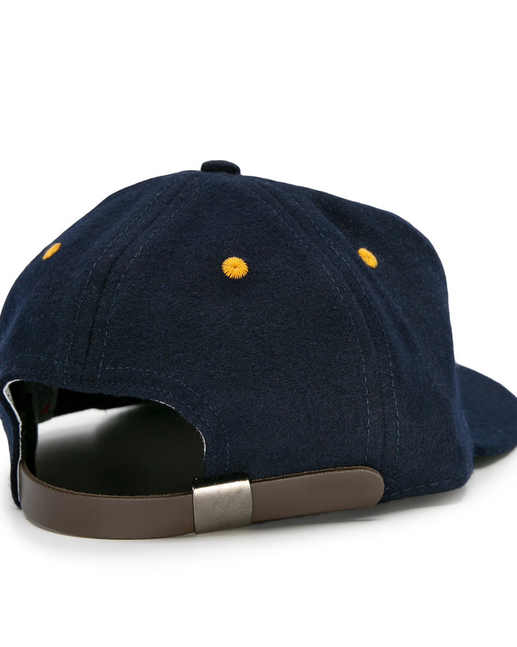 The EFF Great Lakes Naval Station 1944 Vintage Ballcap is a navy wool cap with yellow stitched eyelets, a brown adjustable strap, and a metal clasp, capturing the authentic look of classic 1940s baseball caps.