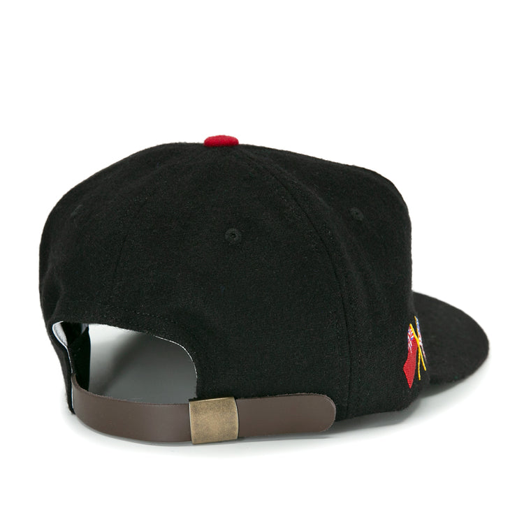 The EFF Galt Terriers 1961 Vintage Ballcap is a black wool hockey cap viewed from the back, with an adjustable brown leather strap, brass buckle, and a small red and yellow Allan Cup-inspired embroidered design on the side.