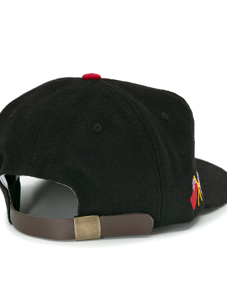 The EFF Galt Terriers 1961 Vintage Ballcap is a black wool hockey cap viewed from the back, with an adjustable brown leather strap, brass buckle, and a small red and yellow Allan Cup-inspired embroidered design on the side.