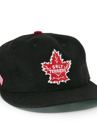 The EFF Galt Terriers 1961 Vintage Ballcap is a black wool cap featuring a red and white maple leaf Galt Terriers logo on the front and crossed Canadian and American flags on the side, honoring Ontario Senior Hockey League history.