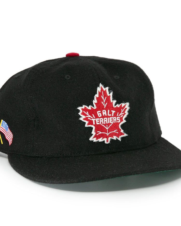 The EFF Galt Terriers 1961 Vintage Ballcap is a black wool cap featuring a red and white maple leaf Galt Terriers logo on the front and crossed Canadian and American flags on the side, honoring Ontario Senior Hockey League history.