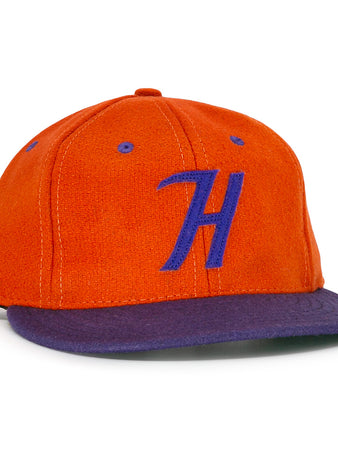 The Hershey Sport Club 1956 Vintage Ballcap by Ebbets Field Flannels features an orange wool build, purple brim, and a bold purple H, inspired by the classic 1956 Hershey ballcap.