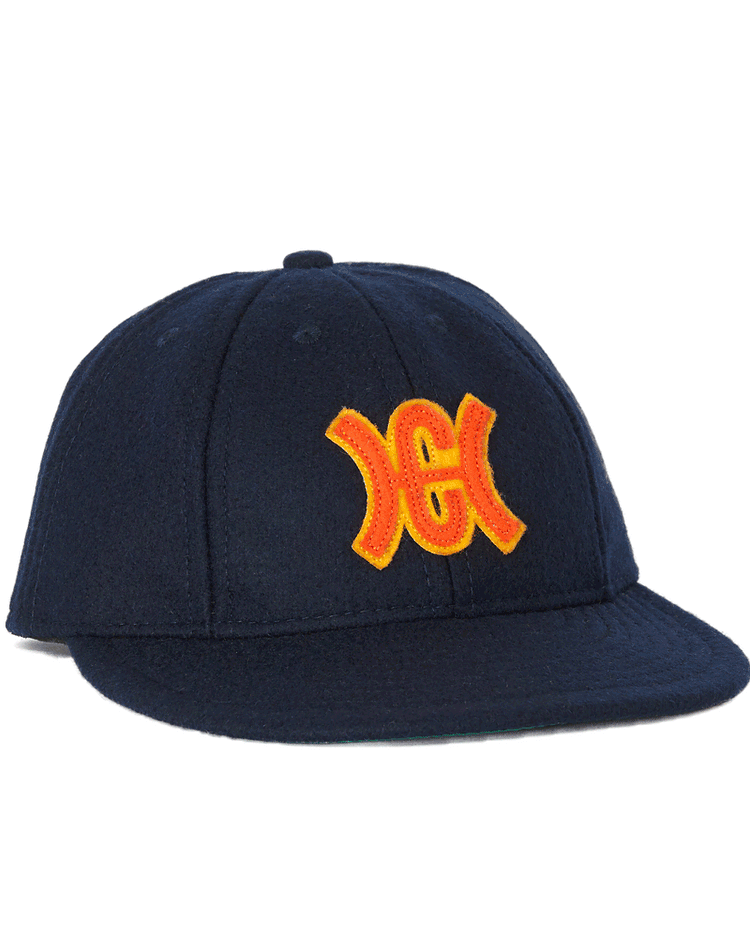 The Ebbets Field Flannels Hiroshima Carp 1959 Vintage 8-panel Ballcap is a dark navy blue cap with a flat brim, yellow-orange embroidered logo, visible stitching, and classic Japanese baseball style, shown angled from the left.
