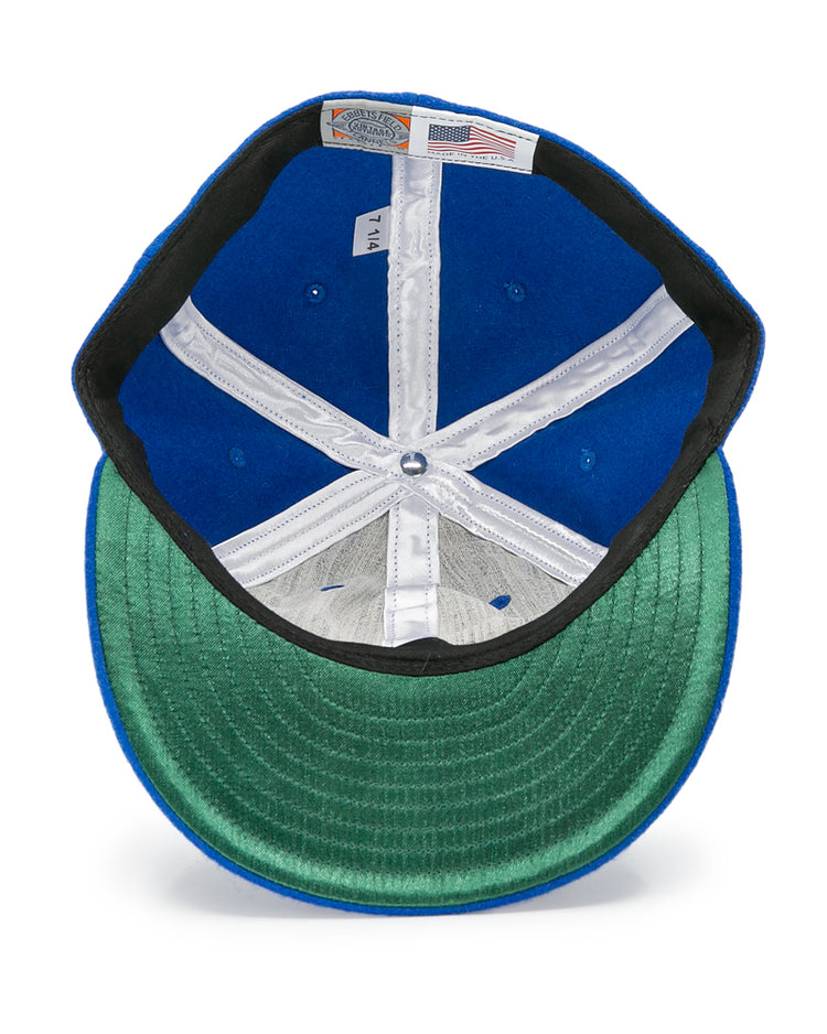 A top-down view shows the inside of the EFF Houston Buffs 1960 Vintage Ballcap, highlighting its blue wool fabric, green underbill, white stitching, plus size and American flag labels.