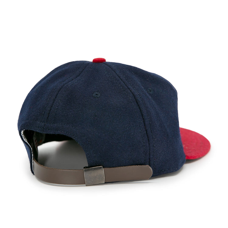 The Jacksonville Braves 1953 Vintage Ballcap by Ebbets Field Flannels is a navy blue cap with a red brim and top button, shown from the back with an adjustable brown leather strap and metal clasp.