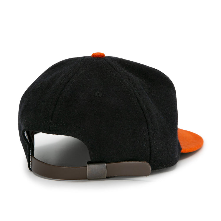 The EFF Jersey City Skeeters 1928 Vintage Ballcap is a black wool cap with an orange visor, shown from the back and featuring an adjustable brown leather strap with a metal buckle.