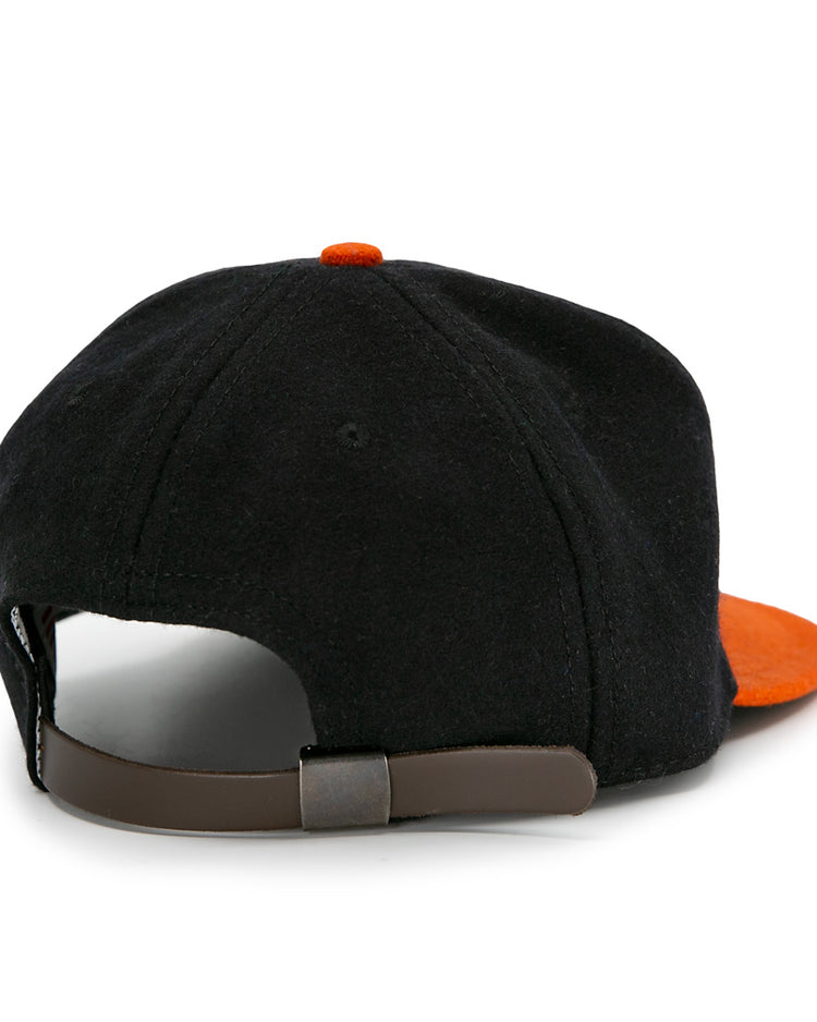 The EFF Jersey City Skeeters 1928 Vintage Ballcap is a black wool cap with an orange visor, shown from the back and featuring an adjustable brown leather strap with a metal buckle.