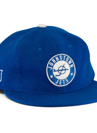 The EFF Johnstown Jets 1970 Vintage Ballcap is royal blue wool with a white circular Jets logo front, EHL shield on the side, white top button, flat brim, and adjustable leather strap for a classic Eastern Hockey League style.