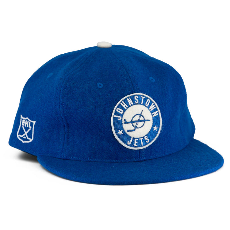 The EFF Johnstown Jets 1970 Vintage Ballcap is royal blue wool with a white circular Jets logo front, EHL shield on the side, white top button, flat brim, and adjustable leather strap for a classic Eastern Hockey League style.