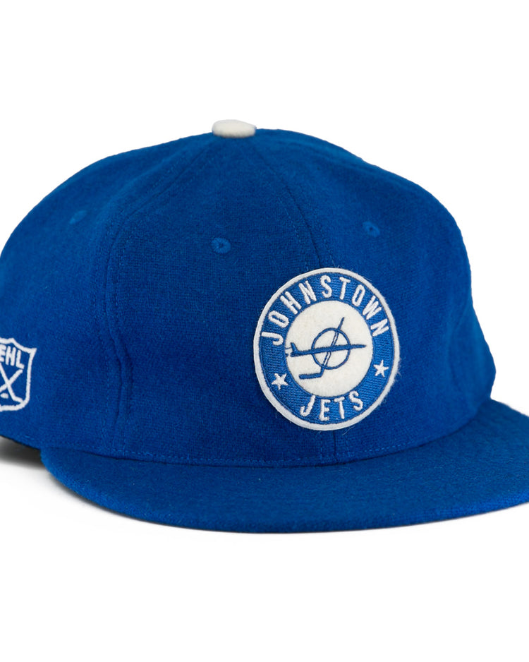 The EFF Johnstown Jets 1970 Vintage Ballcap is royal blue wool with a white circular Jets logo front, EHL shield on the side, white top button, flat brim, and adjustable leather strap for a classic Eastern Hockey League style.