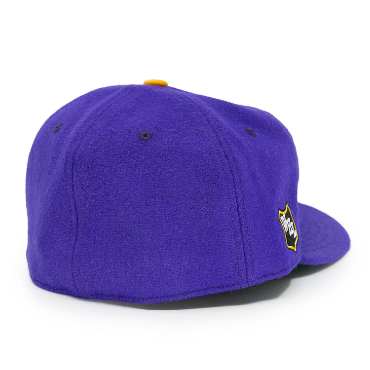 The EFF Los Angeles Monarchs 1947 Vintage Ballcap is a purple wool cap with a yellow top button, small ventilation holes, and a yellow and black shield logo on the side, shown from the back-left angle.