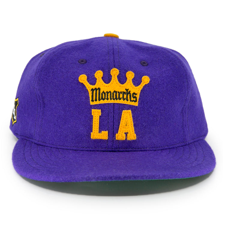 The EFF Los Angeles Monarchs 1947 Vintage Ballcap is a purple wool hat with a yellow crown, featuring Monarchs above bold yellow LA letters on the front, honoring the teams Western Hockey League history.
