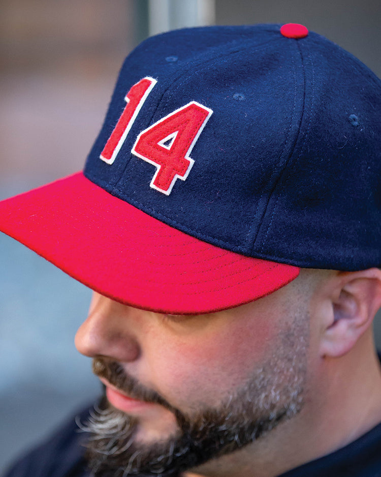 A man with a trimmed beard wears an Ebbets Field Flannels Larry Doby Signature Series Ballcap in navy blue, featuring a red brim and the number 14 in red and white on the front.