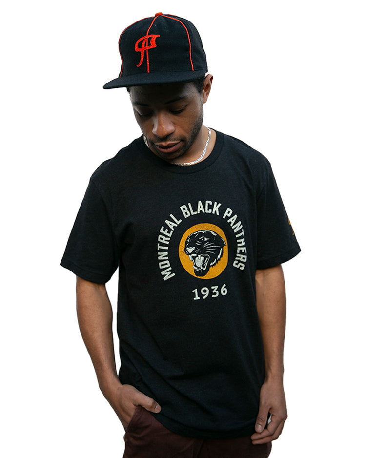 A man in an EFF Montreal Black Panthers 1936 Vintage Ballcap and a matching black T-shirt with the team name and panther logo stands against a white background, looking down.