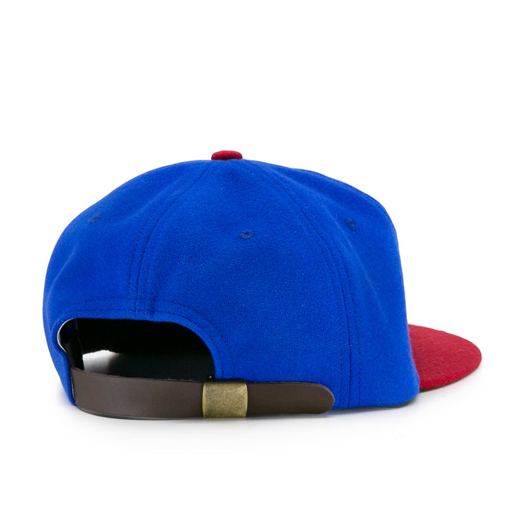The EFF Montreal Royals 1935 Vintage Ballcap features a blue crown, red brim, and a brown adjustable strap with brass buckle, viewed from the back—a classic homage to baseball history.