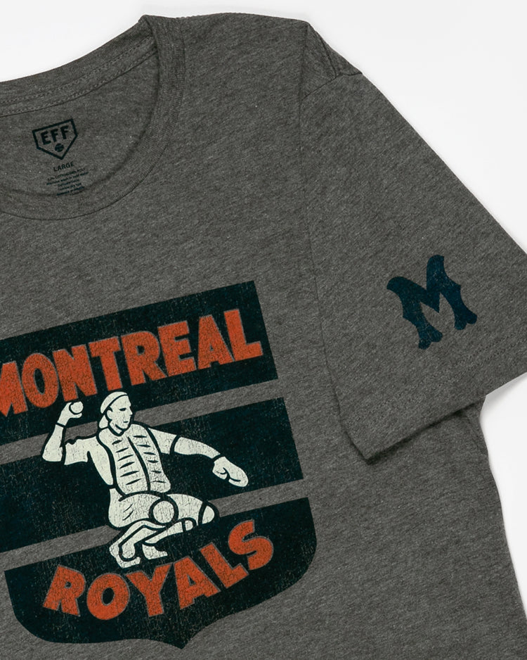 The EFF Montreal Royals 1946 T-Shirt is a gray tee with a graphic of a catcher in gear, Montreal Royals text in orange and cream, and a large blue M on the left sleeve—honoring Dodgers prospect Roberto Clemente.