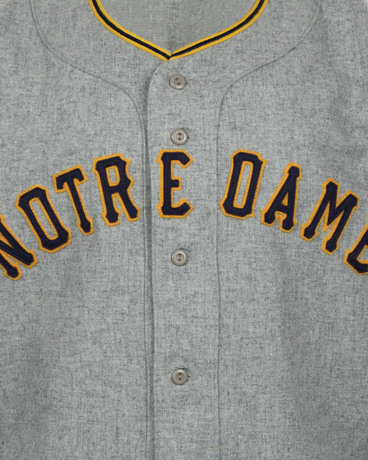 The EFF University of Notre Dame 1956 Road Jersey features gray flannel with yellow and navy trim, plus bold yellow NOTRE DAME lettering outlined in navy for a classic Collegiate Team Authentic style.