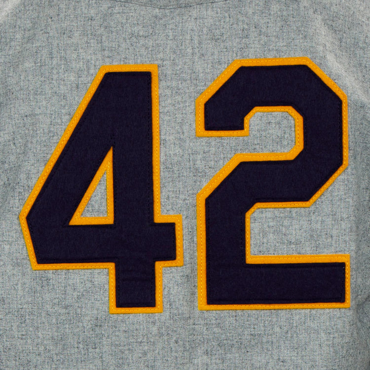 A large dark blue number 42 outlined in yellow is sewn onto gray fabric, echoing the classic style of the EFF University of Notre Dame 1956 Road Jersey.